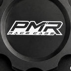 A black anodized aluminum fuel cell cap with a white and black PMR logo in the center and pre-drilled bolt holes around the outer rim, shown on a white background.