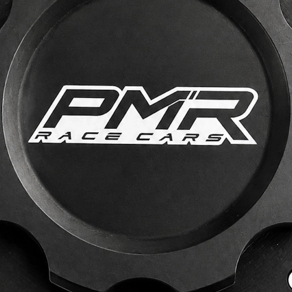 A black anodized aluminum fuel cell cap with a white and black PMR logo in the center and pre-drilled bolt holes around the outer rim, shown on a white background.