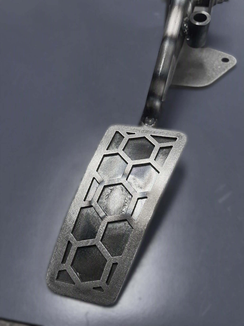 A close-up of the PMR Camaro COPO accelerator pedal with a hexagonal cutout pattern on a dark gray surface.